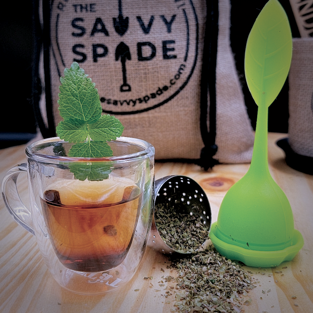 A cup of tea in a clear glass mug with the Savvy Spade burlap gift bag in the background